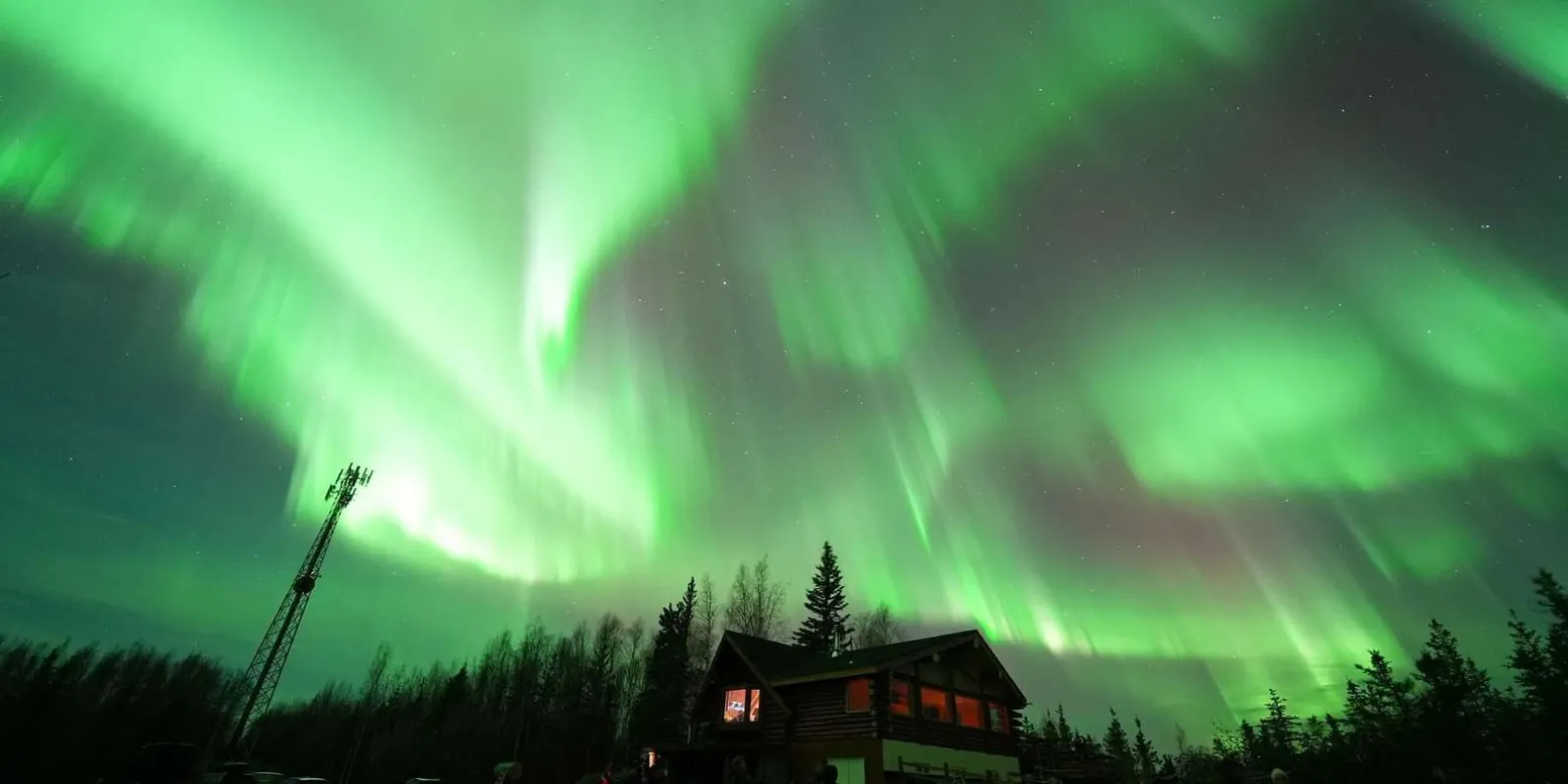 Green aurora sweeping across the sky above the Aurora Husky Lodge cabin and radio tower