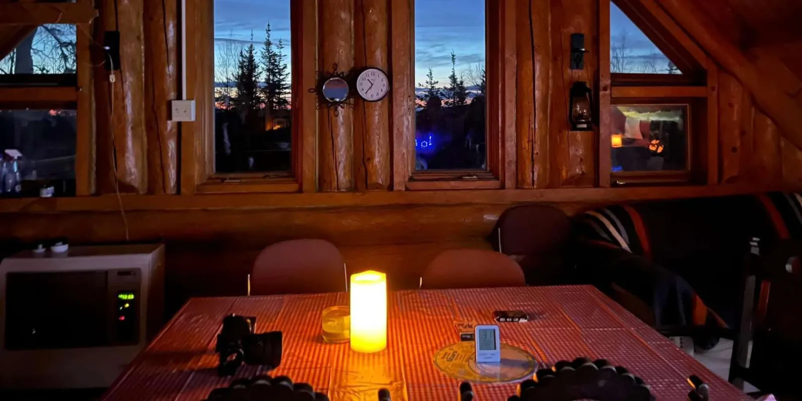 Cozy cabin interior with a lit candle on a wooden table and dusk views through log-cabin windows