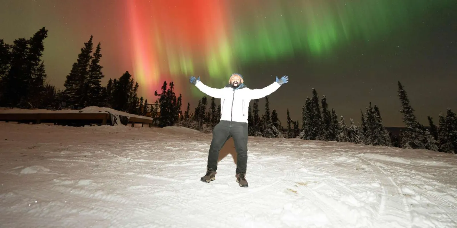 Guest with arms raised on the deck under a red and green aurora at Cleary Summit