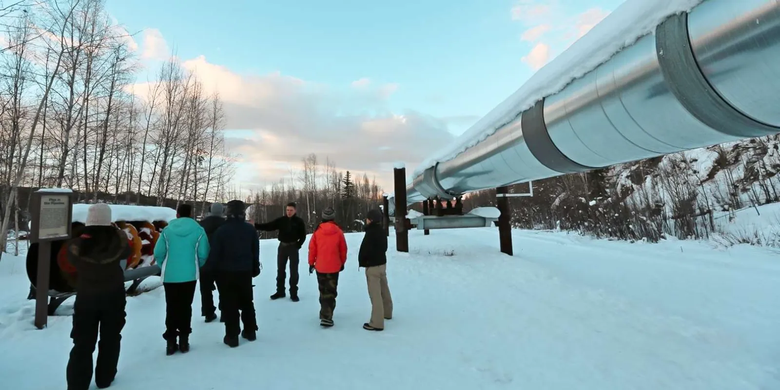 Small group of travelers viewing the elevated Trans-Alaska Pipeline in the snow