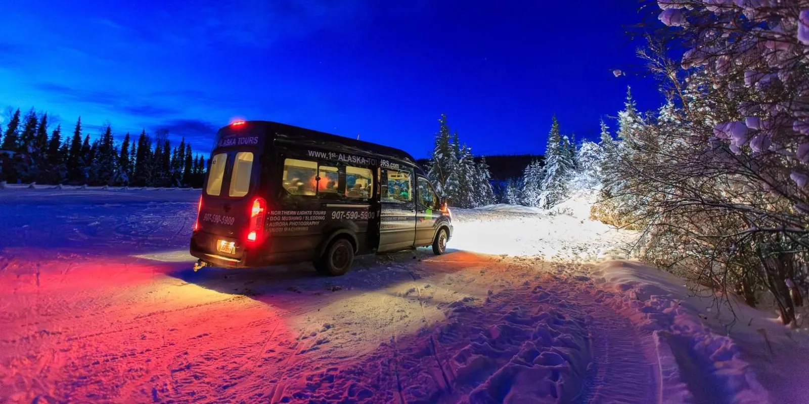 Tour van branded for northern lights tours and dog mushing parked at dusk in the snow