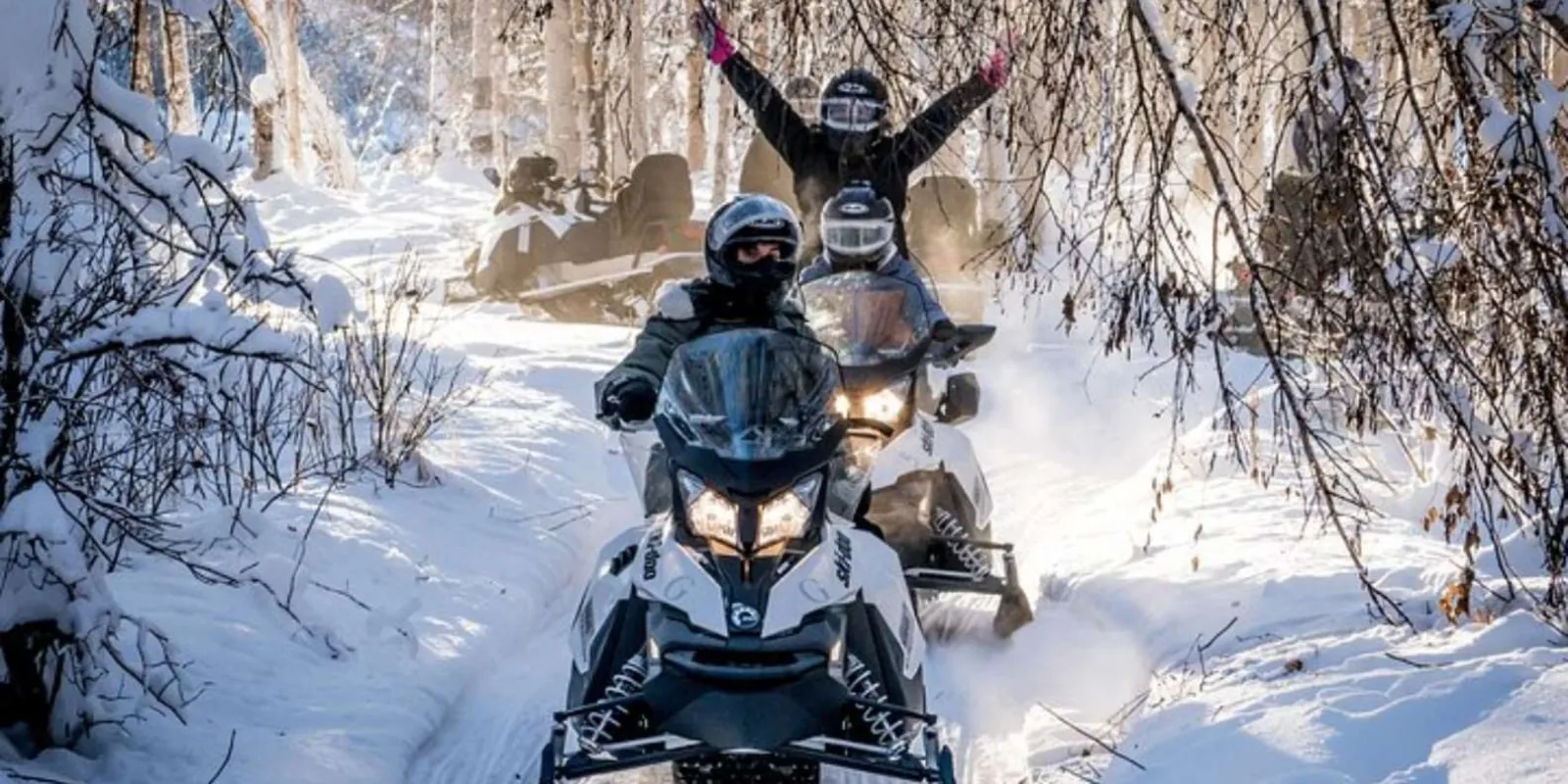 Smiling rider raising both arms on a snowmobile trail in the winter forest near Fairbanks