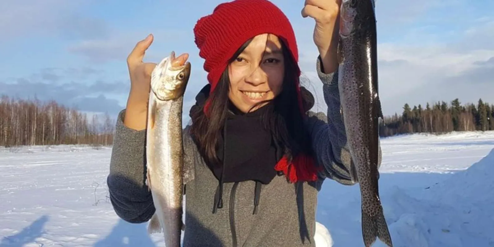 Smiling angler in a red hat holding two fish on a frozen lake outside Fairbanks